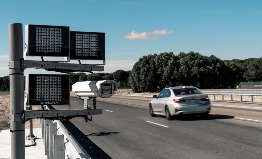 Indra's DAVAO camera and tolling technology stands at the edge of a highway as cars drive past.